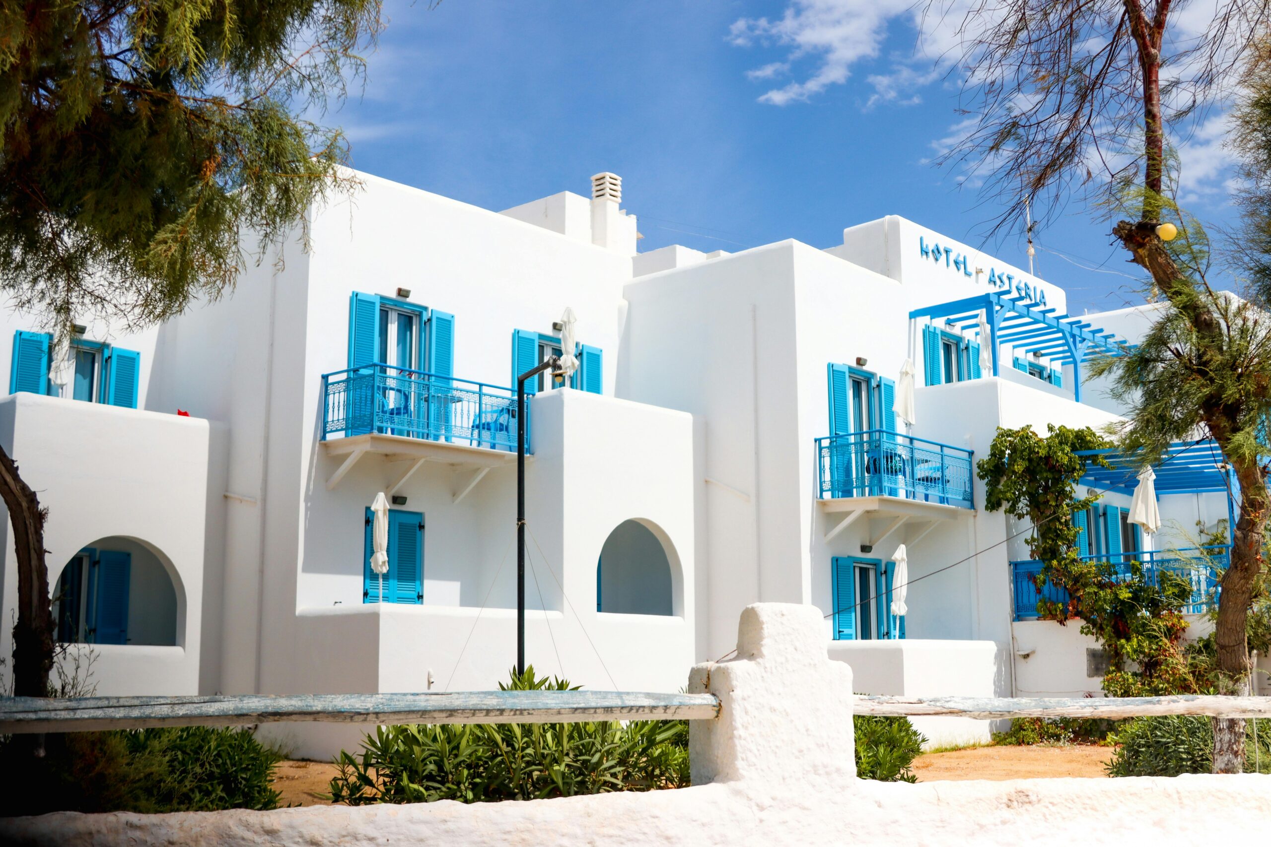 Whitewashed Greek hotel with blue shutters in Naxos under a clear sky.